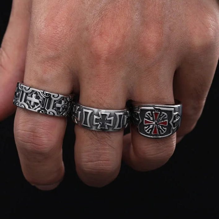 Three metallic rings with intricate designs on a person's hand against a dark background