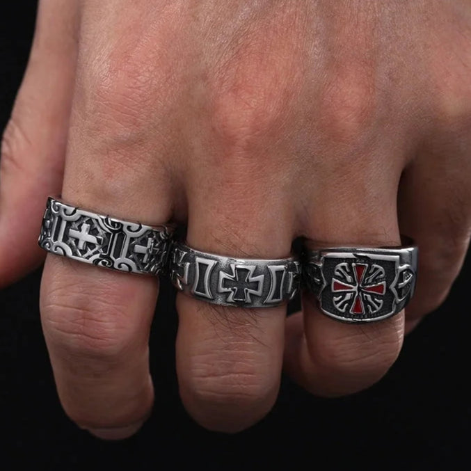 Three metallic rings with intricate designs on a person's hand against a black background