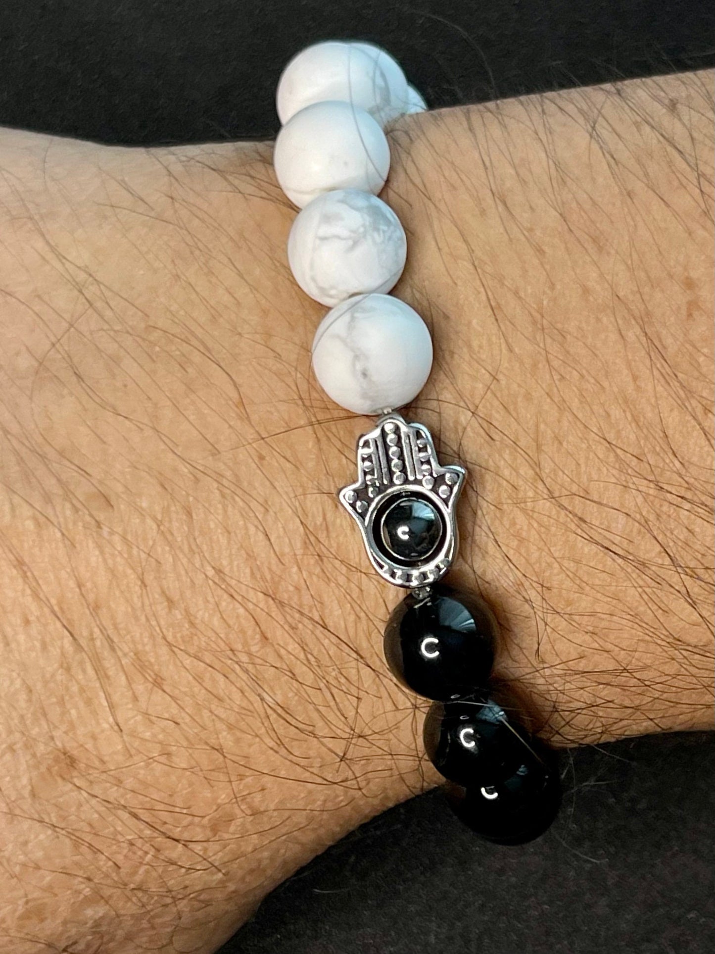 Elegant black and white stretch bead bracelet set with Buddha charm, cross pendant, and Hamsa hand symbol styled on a dark background for a luxury jewelry look.