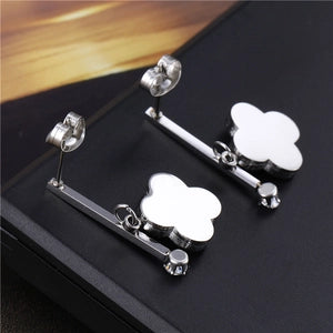 Silver flower-shaped earrings on a black stand with a blurred wooden surface in the background.