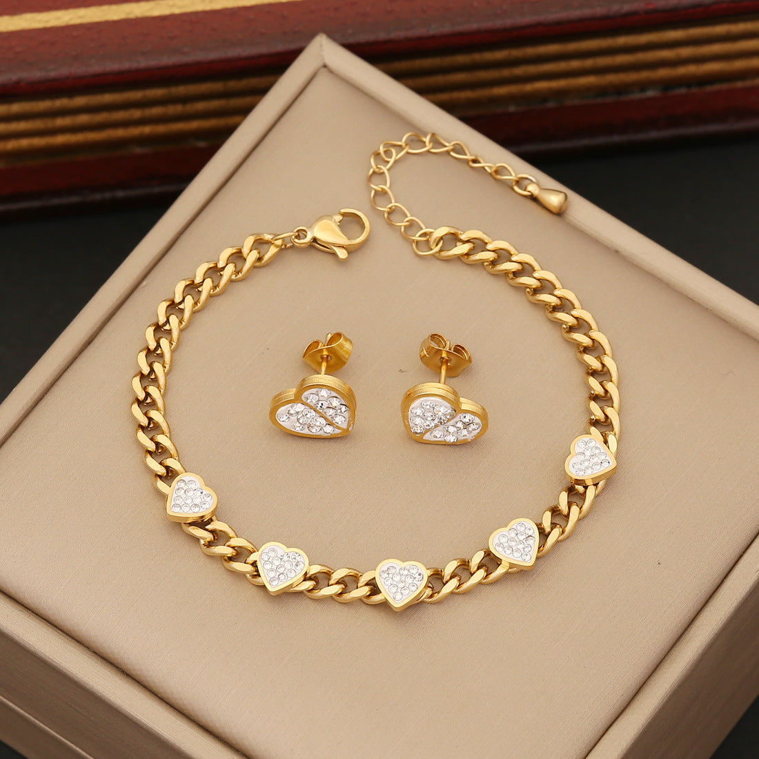 Gold bracelet and heart-shaped earrings on a beige jewelry box