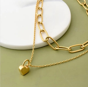 Gold chain necklace with a heart-shaped lock pendant on a green surface.