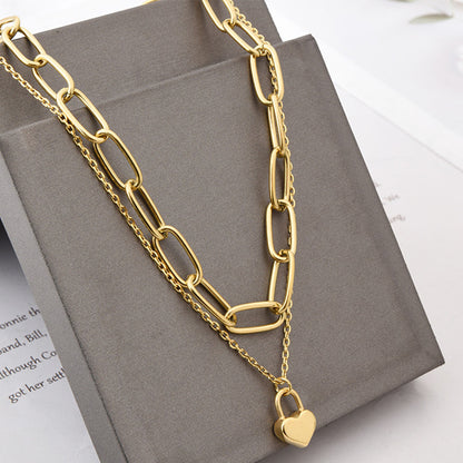 Gold chain necklace with a heart-shaped lock pendant on a gray box.