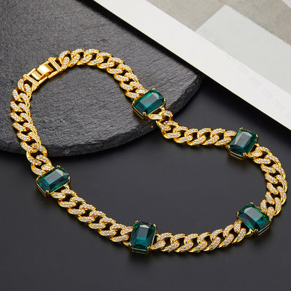 Gold chain bracelet with green gemstones on a dark surface