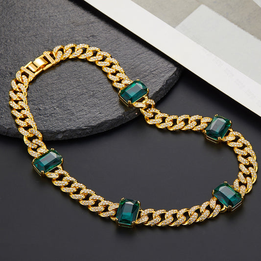 Gold chain bracelet with green gemstones on a dark surface