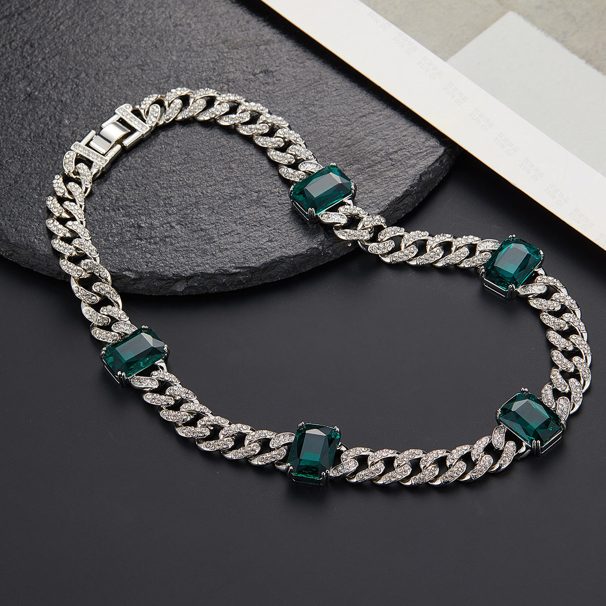 Silver chain necklace with green gemstones on a dark surface