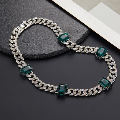 Silver chain necklace with green gemstones on a dark surface