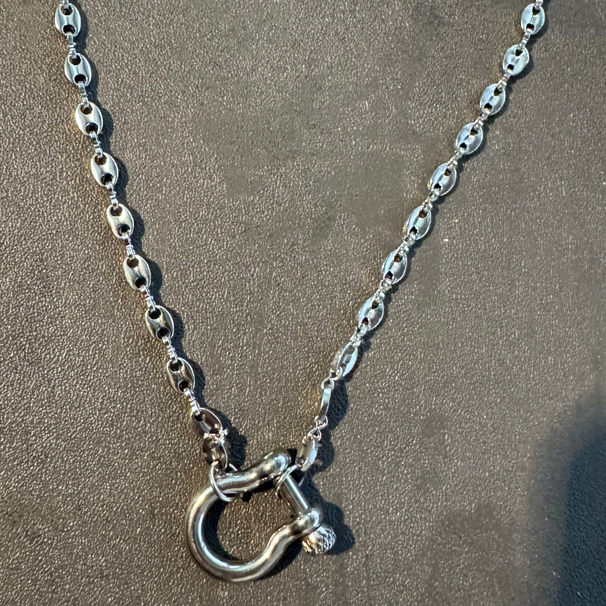 Silver chain necklace with a clasp on a sandy surface