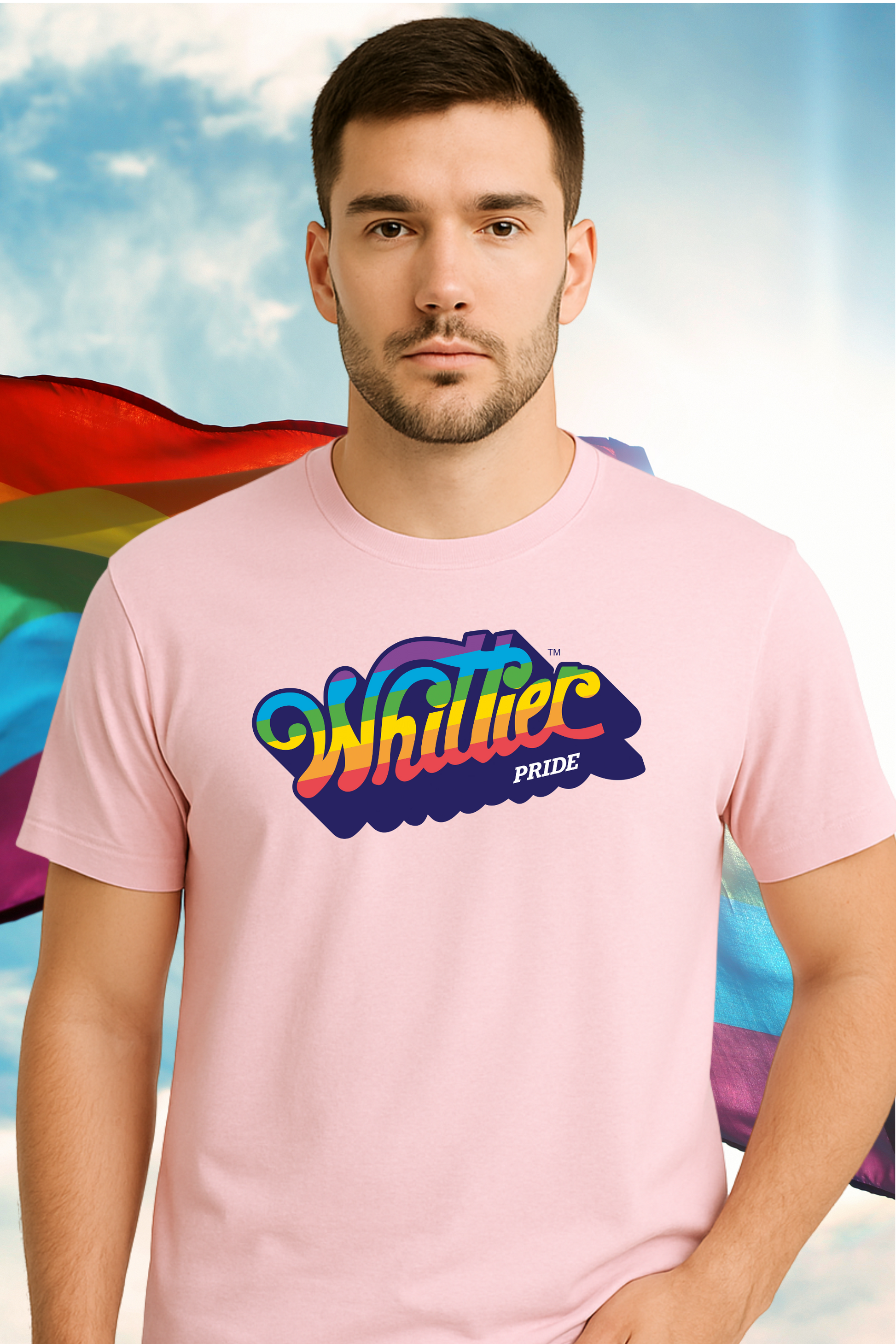 Man wearing a pink t-shirt with 'Whittle Pride' design against a rainbow flag and blue sky background