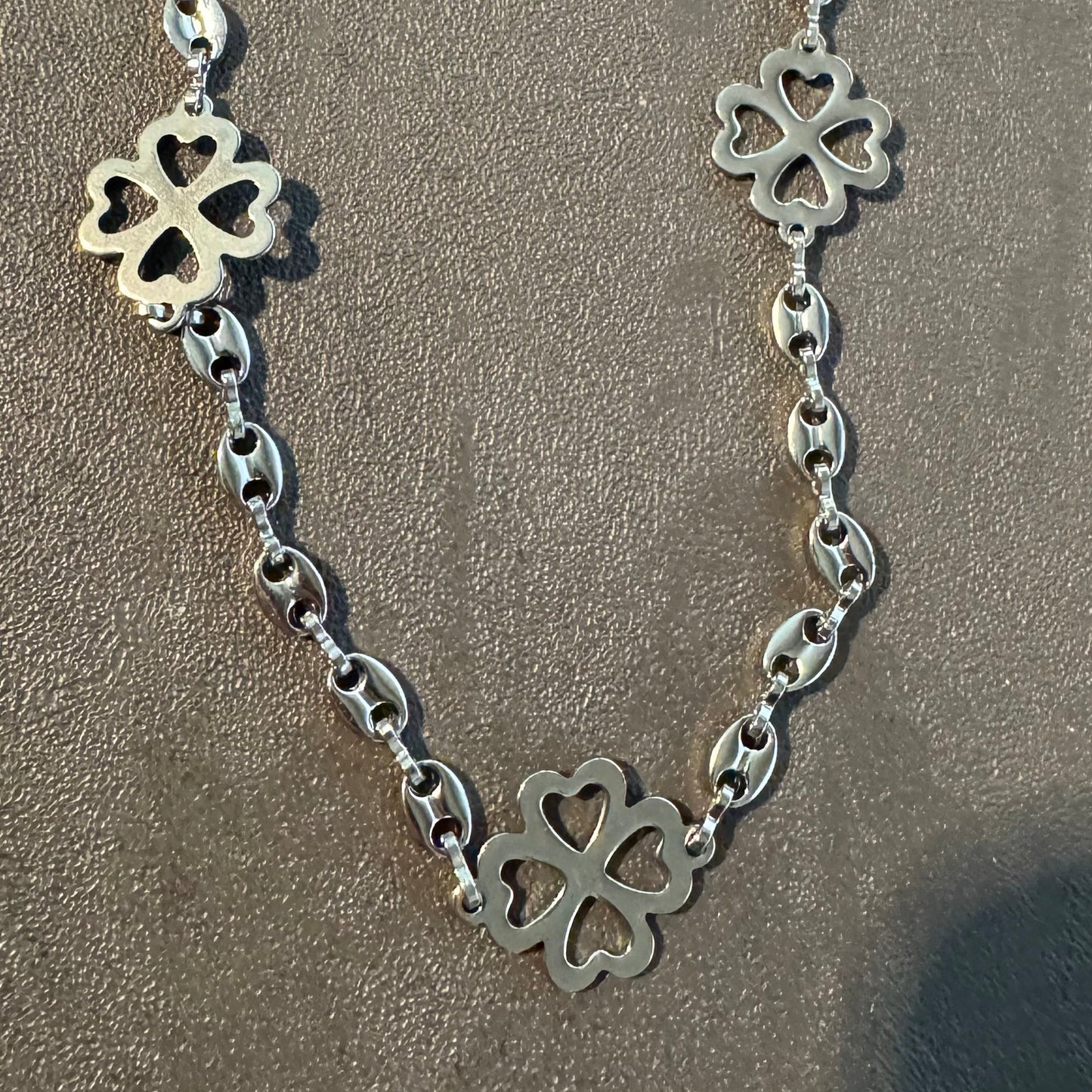 Silver necklace with clover-shaped pendants on a sandy background