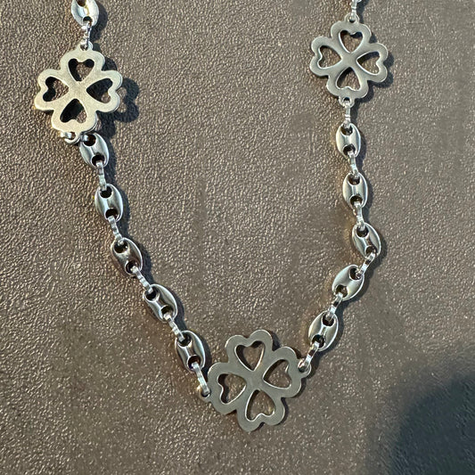 Silver necklace with clover-shaped pendants on a sandy background