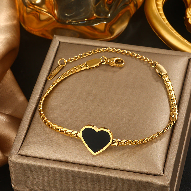 Gold bracelet with a heart-shaped black stone on a brown box, with a gold perfume bottle in the background.
