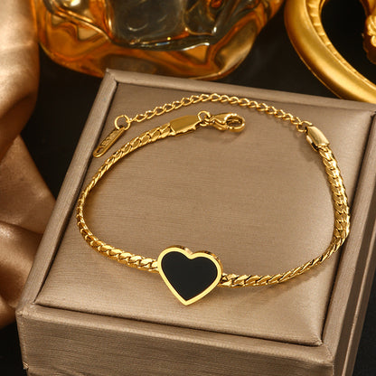 Gold bracelet with a heart-shaped black stone on a brown box, with a gold perfume bottle in the background.