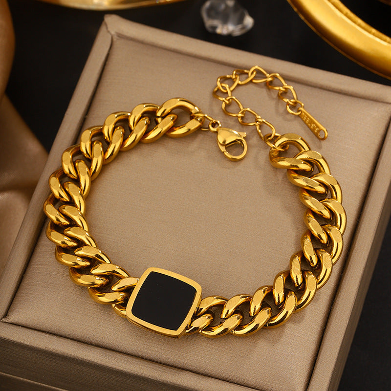 Gold chain bracelet with a black square clasp on a beige jewelry box.