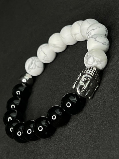 Spiritual black and white gemstone bracelet with polished black beads, white marbled howlite stones, silver Buddha head charm and symbolic cross and Hamsa accents.